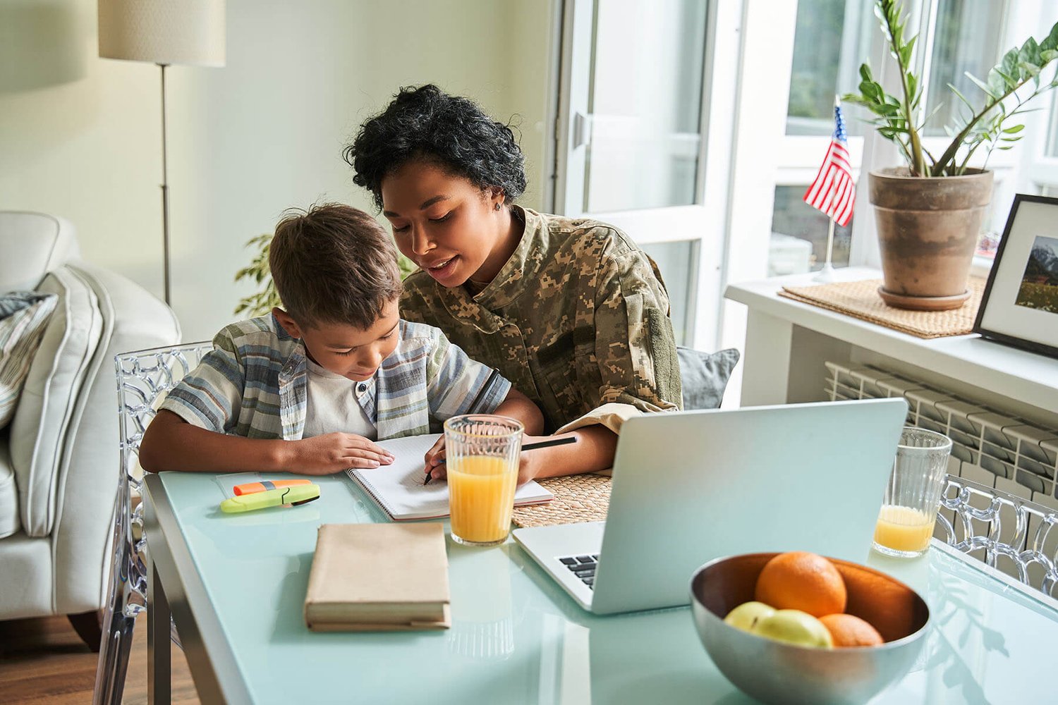 servicewoman in uniform helping her child with homework at the breakfast table